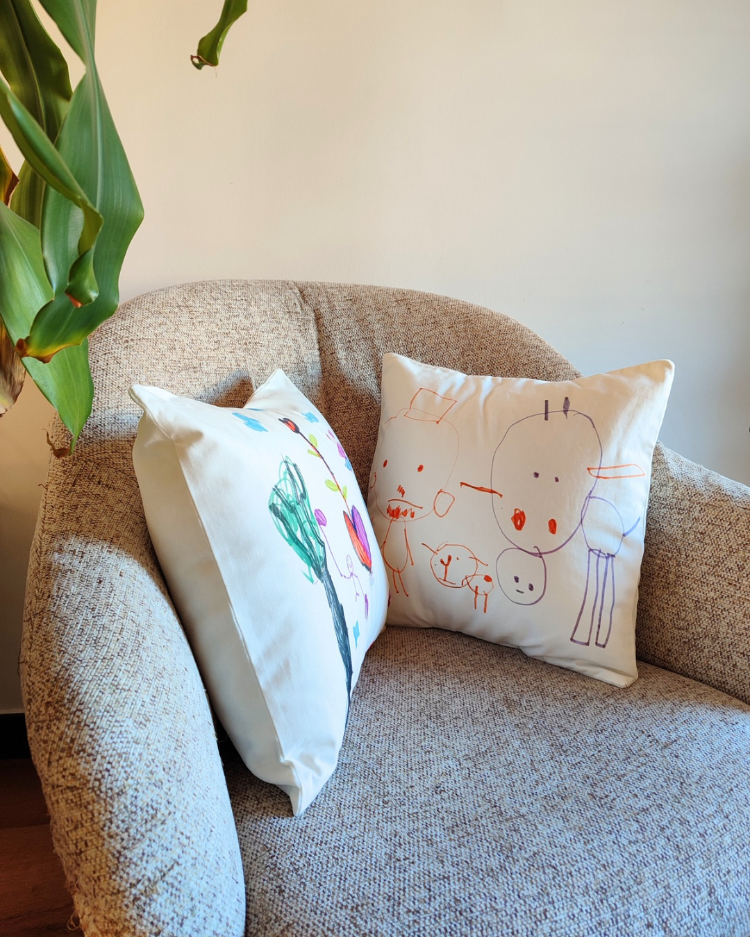 due cuscini quadrati 40x40 cm posizionati su una poltrona color sabbia. i cuscini completamente sfoderatili presentano sul lato anteriore i disegni a pennarello di due bambini. i disegni sono colorati su sfondo bianco.